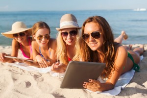 group of smiling young women with tablets on beach